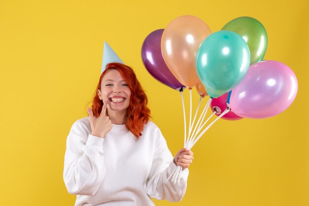 Vista frontale della giovane donna che tiene palloncini colorati sulla parete gialla