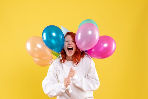 Vista frontale della giovane donna che tiene palloncini colorati sulla parete gialla