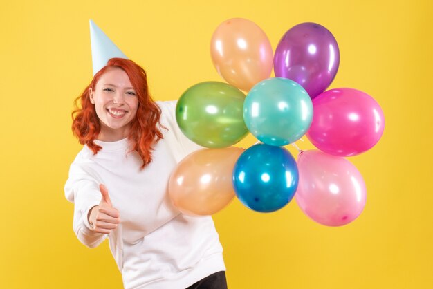 Vista frontale della giovane donna che tiene palloncini colorati sulla parete gialla