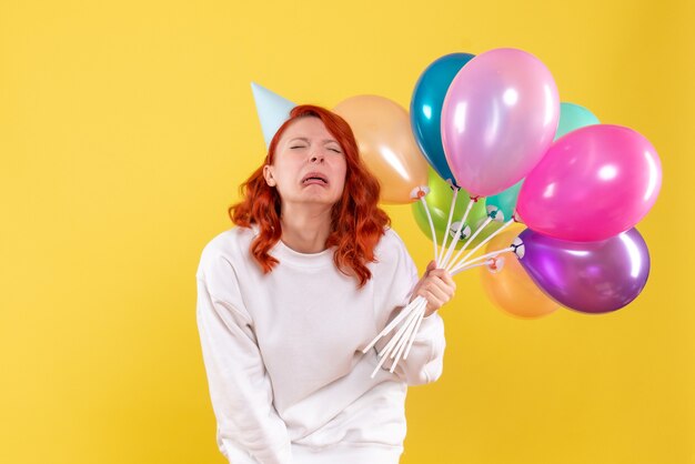 Vista frontale della giovane donna che tiene palloncini colorati sulla parete gialla