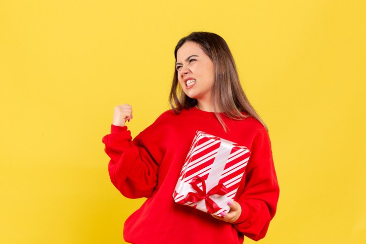 Foto gratuito vista frontale della giovane donna che tiene piccolo regalo e che si rallegra sulla parete gialla