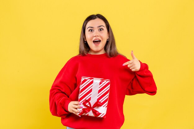 Vista frontale della giovane donna che tiene piccolo regalo su una parete gialla