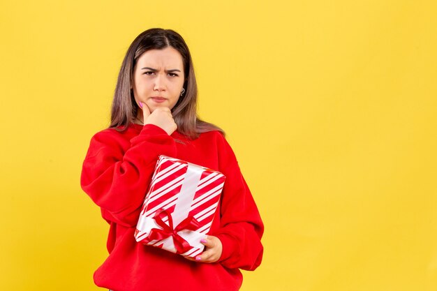 Vista frontale della giovane donna che tiene piccolo regalo su una parete gialla