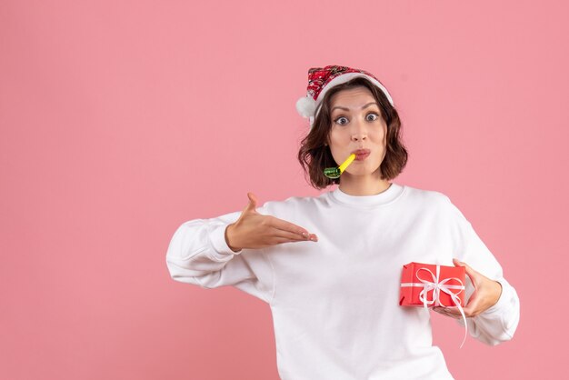 Vista frontale della giovane donna che tiene poco natale presente sulla parete rosa