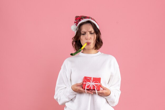 Vista frontale della giovane donna che tiene poco natale presente sulla parete rosa