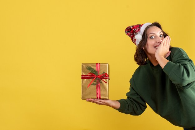 Vista frontale della giovane donna che tiene poco regalo di Natale sulla parete gialla