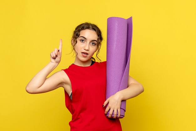 Vista frontale della giovane donna che tiene tappeto viola sul muro giallo chiaro