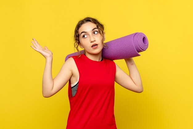 Vista frontale della giovane donna che tiene tappeto viola sulla parete gialla