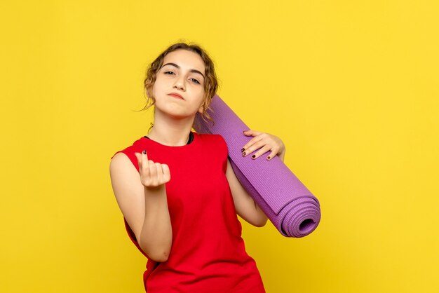 Vista frontale della giovane donna che tiene tappeto viola sulla parete gialla