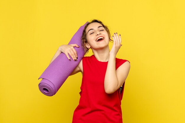 Vista frontale della giovane donna che tiene tappeto viola sulla parete gialla