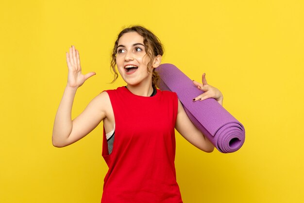 Vista frontale della giovane donna che tiene tappeto viola sulla parete gialla