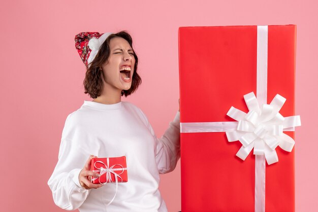 Vista frontale della giovane donna che tiene un piccolo regalo di Natale con uno enorme sulla parete rosa