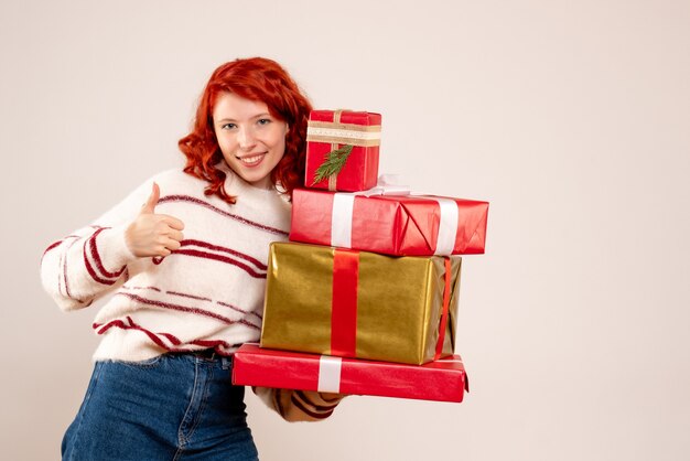 Vista frontale della giovane donna che trasportano i regali di Natale sul muro bianco