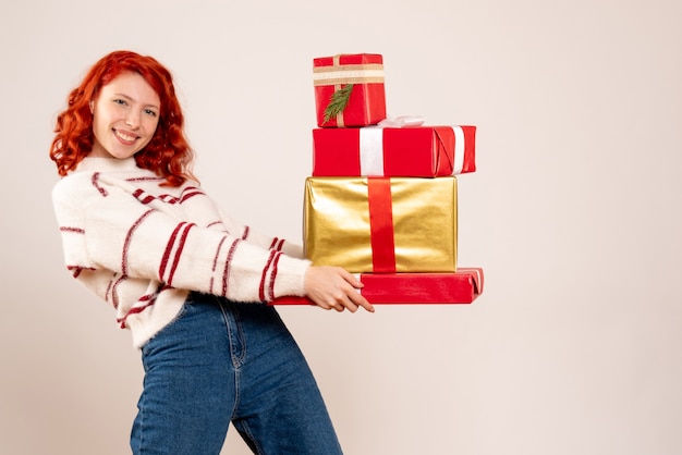 Vista frontale della giovane donna che trasportano i regali di Natale sul muro bianco