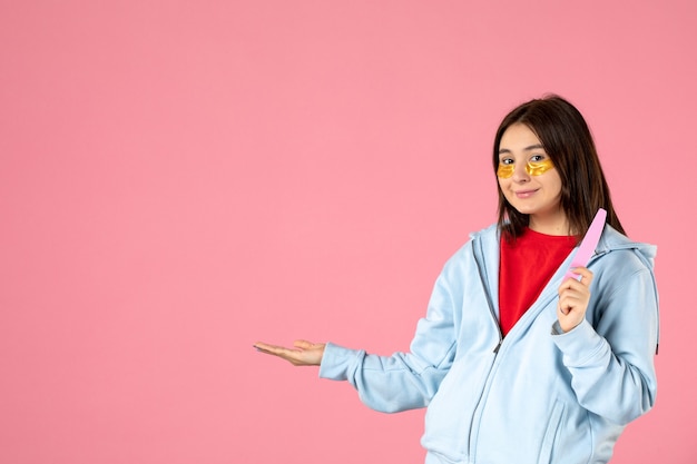 vista frontale della giovane donna con bende per gli occhi e lima per unghie sul muro rosa