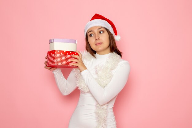 Vista frontale della giovane donna con berretto rosso che tiene regali a forma di cuore sulla parete rosa