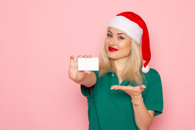 Vista frontale della giovane donna con berretto rosso che tiene una carta bianca sul muro rosa