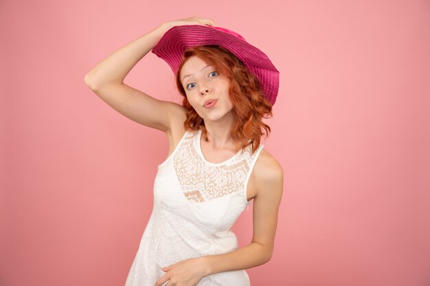 Vista frontale della giovane donna con cappello rosa sulla parete rosa chiaro