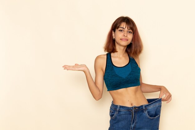 Vista frontale della giovane donna con corpo in forma in camicia blu sorridente sul muro bianco chiaro