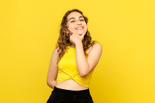Vista frontale della giovane donna con espressione sorridente sul muro giallo