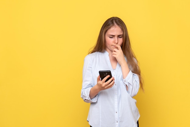 Vista frontale della giovane donna con il telefono sul muro giallo