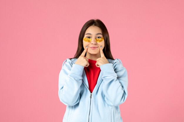 vista frontale della giovane donna con le bende sull'occhio sotto gli occhi sul muro rosa