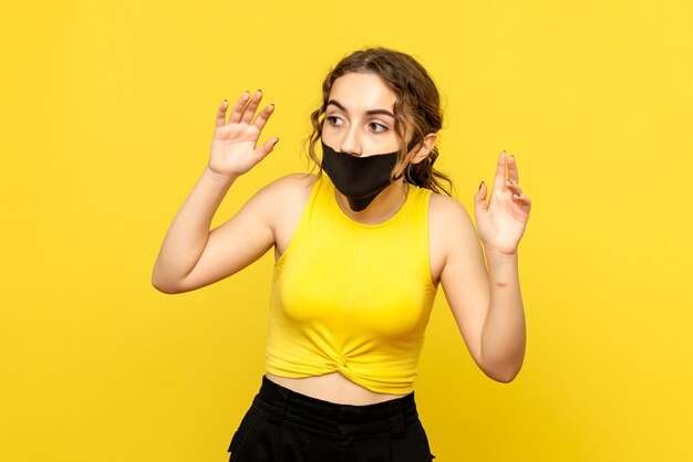 Vista frontale della giovane donna con maschera nera sulla parete gialla