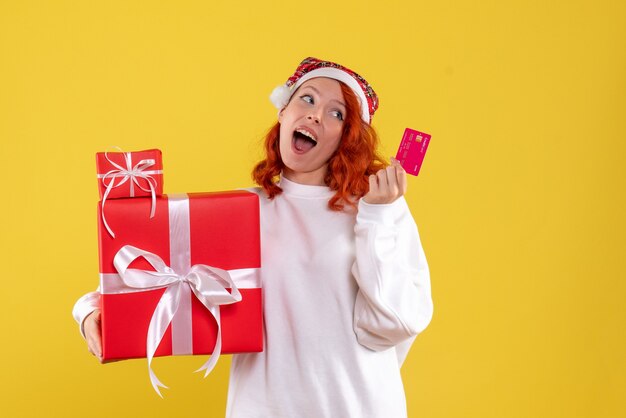 Vista frontale della giovane donna con regali di Natale e carta di credito sulla parete gialla