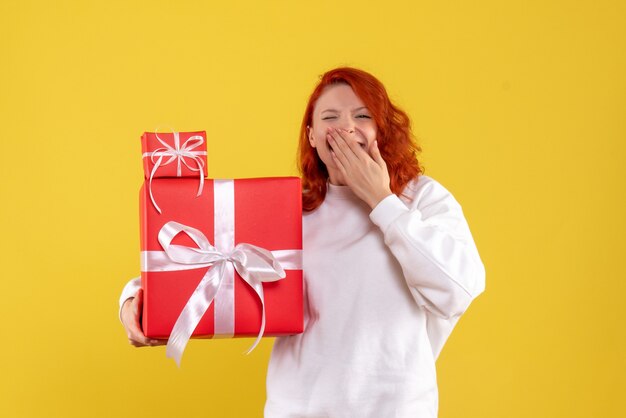 Vista frontale della giovane donna con regali di Natale sulla parete gialla