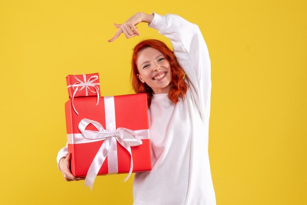 Vista frontale della giovane donna con regali di Natale sulla parete gialla