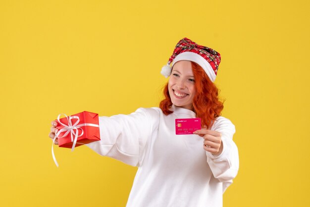 Vista frontale della giovane donna con regalo di Natale e carta di credito sulla parete gialla