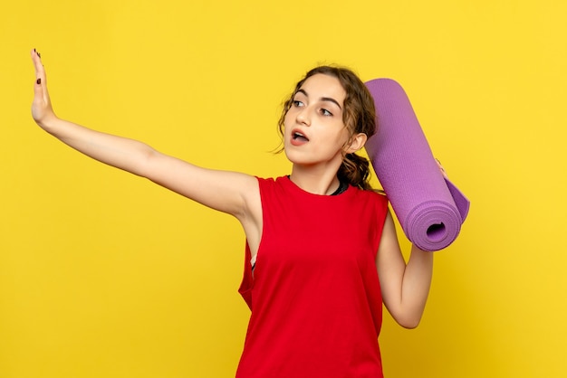 Vista frontale della giovane donna con tappeto viola sulla parete gialla