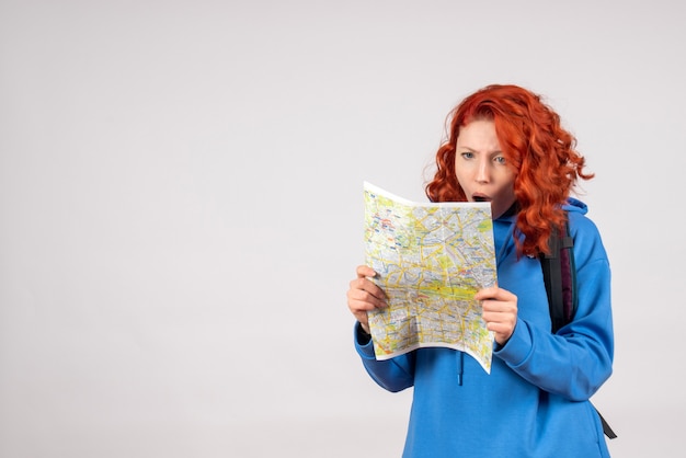 Vista frontale della giovane donna con zaino e mappa sul muro bianco