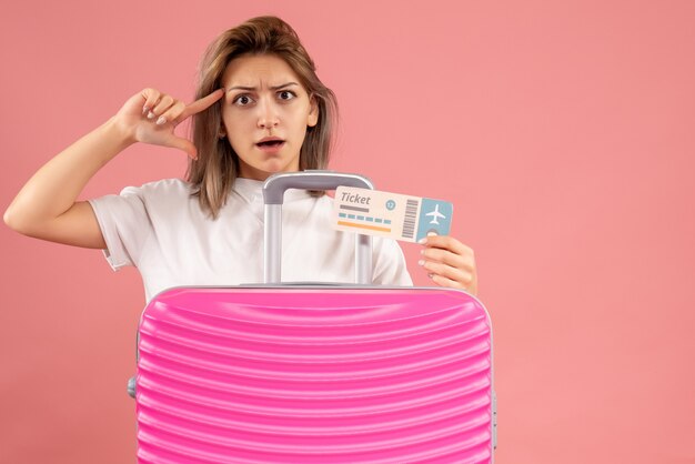 Vista frontale della giovane donna confusa con il biglietto rosa della tenuta della valigia