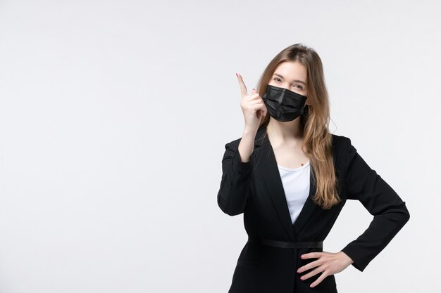 Vista frontale della giovane donna confusa in tuta che indossa maschera chirurgica e punta verso l'alto su bianco