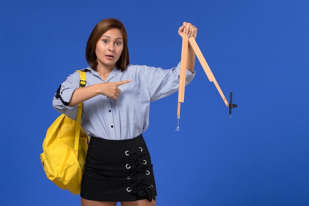 Vista frontale della giovane donna in camicia blu che tiene la figura di legno sulla parete blu