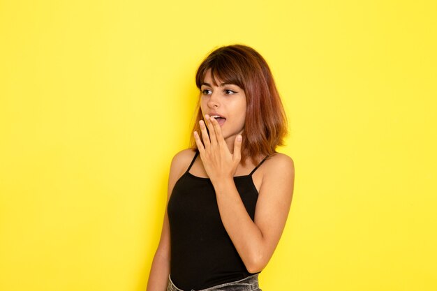 Vista frontale della giovane donna in camicia nera in posa sul muro giallo chiaro