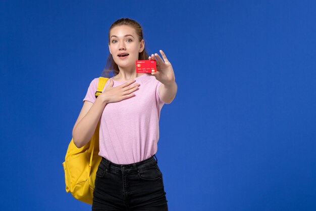 Vista frontale della giovane donna in maglietta rosa che indossa lo zaino giallo che tiene il cartellino rosso di plastica