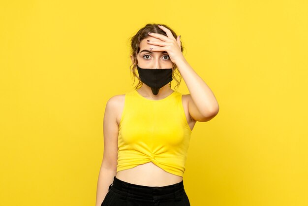 Vista frontale della giovane donna in maschera nera sulla parete gialla
