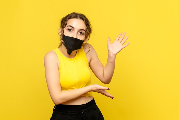 Vista frontale della giovane donna in maschera nera sulla parete gialla