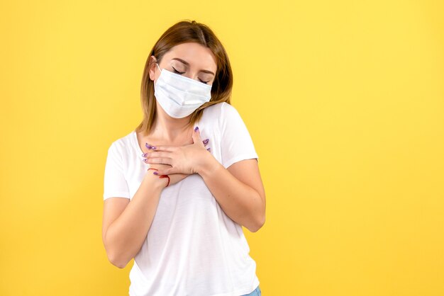 Vista frontale della giovane donna in maschera sterile sulla parete gialla