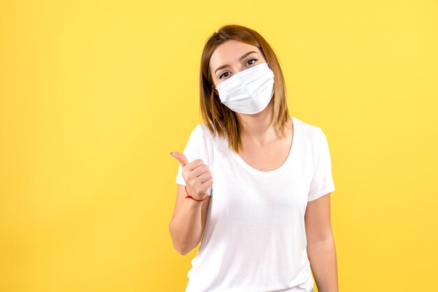 Vista frontale della giovane donna in maschera sterile sulla parete gialla