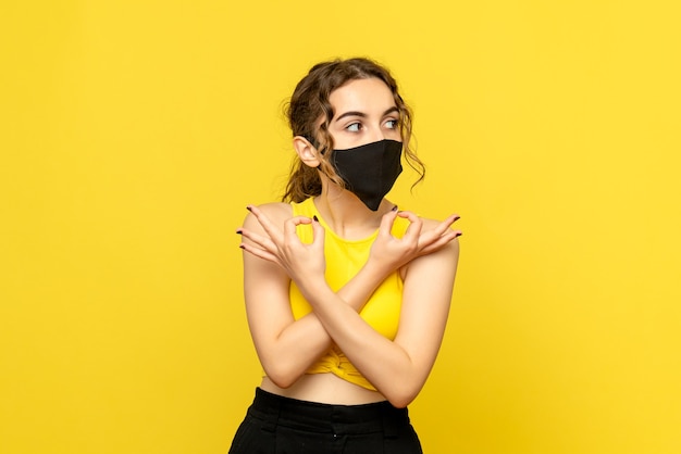 Vista frontale della giovane donna in maschera sulla parete gialla