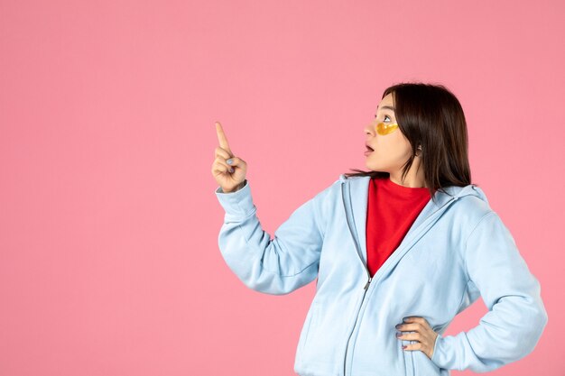 vista frontale della giovane donna in posa con bende per gli occhi sotto gli occhi sul muro rosa