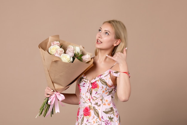 Vista frontale della giovane donna in posa con bouquet di bellissime rose sul muro marrone