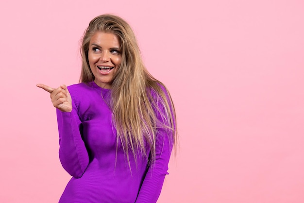 Vista frontale della giovane donna in posa con un bellissimo vestito viola su un muro rosa chiaro