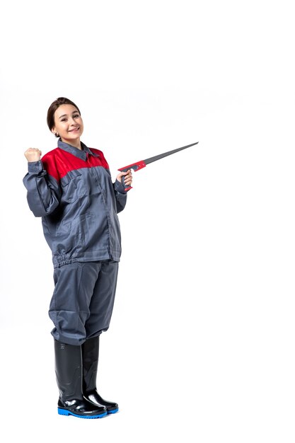 vista frontale della giovane donna in uniforme che tiene il seghetto sul muro bianco