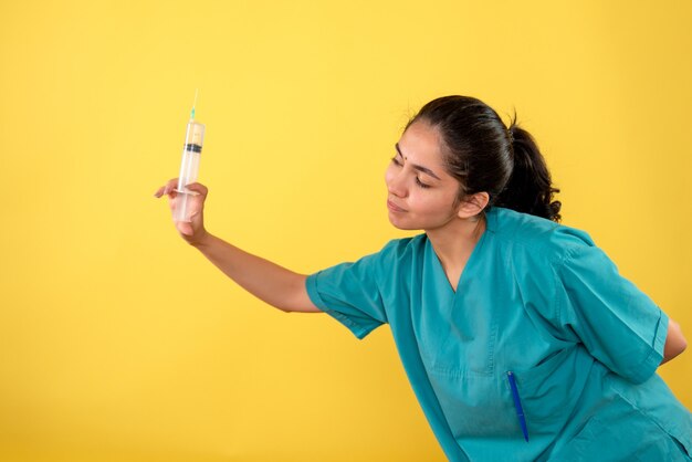 Vista frontale della giovane donna medico tenendo la siringa sulla parete gialla