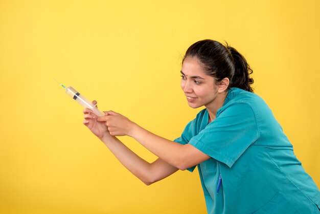 Vista frontale della giovane donna medico utilizzando la siringa sulla parete gialla