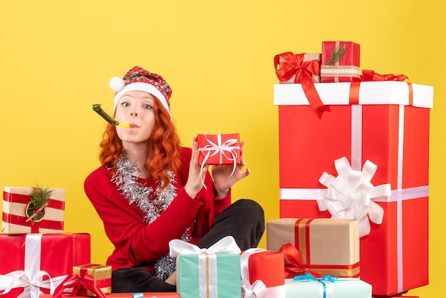 Vista frontale della giovane donna seduta intorno a diversi regali di Natale sulla parete gialla